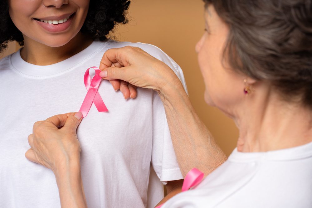 Senior,Volunteer,Applying,Pink,Ribbon,On,Smiling,Young,Woman's,White